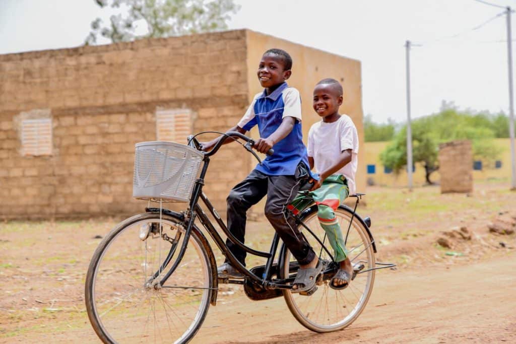 Deux garçons font du vélo sur un chemin de terre au Burkina Faso.