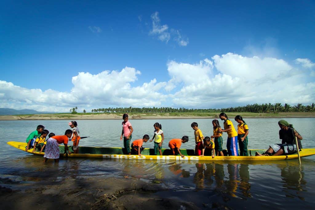 Les enfants montent sur un canoë fabriqué à partir d'un cocotier évidé. Certains sont debout et certains sont assis. 