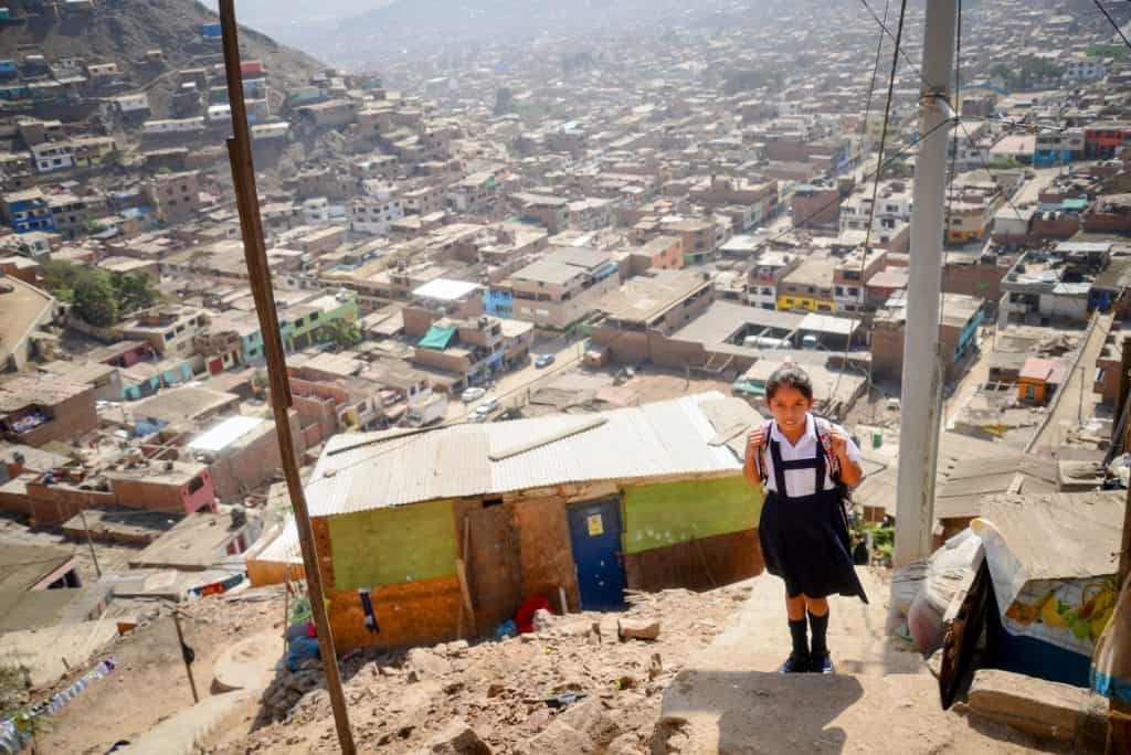 Une fille portant un uniforme scolaire et un sac à dos monte des escaliers raides. Une ville est vue en arrière-plan et en dessous d'elle