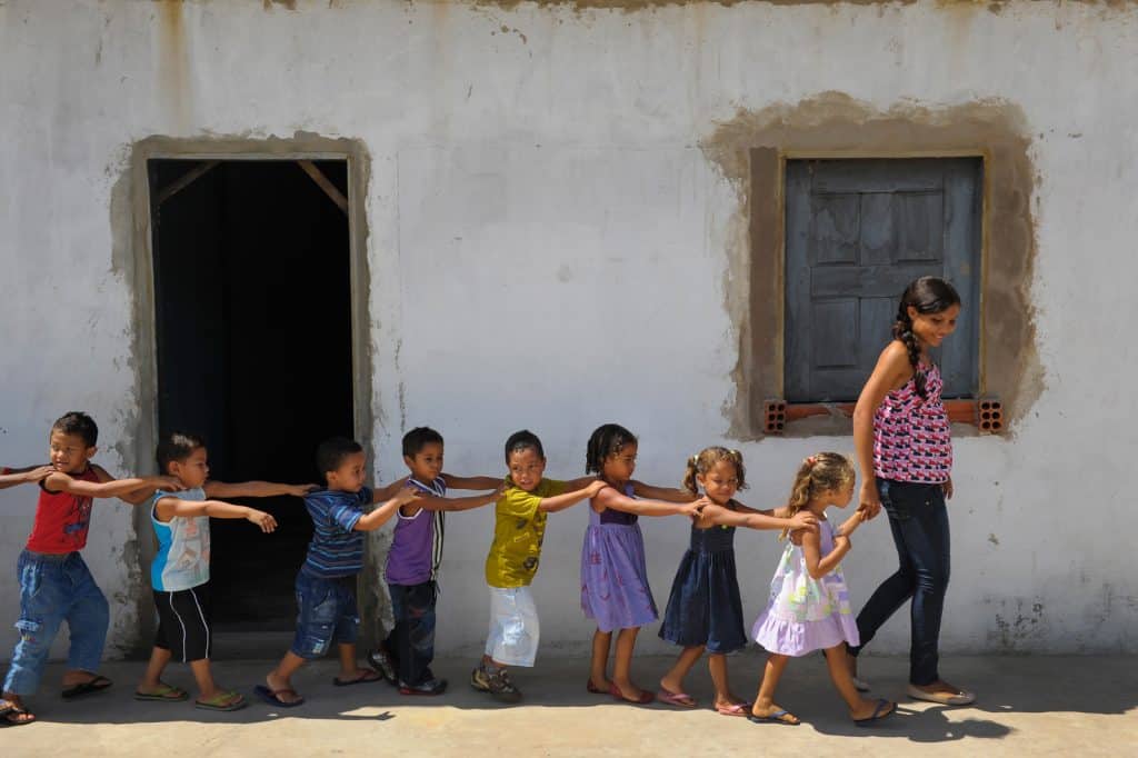 Les enfants s'alignent avec leurs mains sur les épaules en file indienne, à la suite d'un adulte