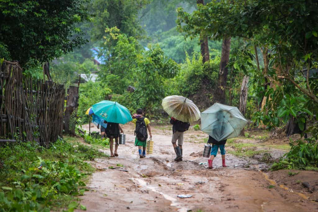 Des enfants tenant des parapluies marchent sous la pluie et la boue en Thaïlande