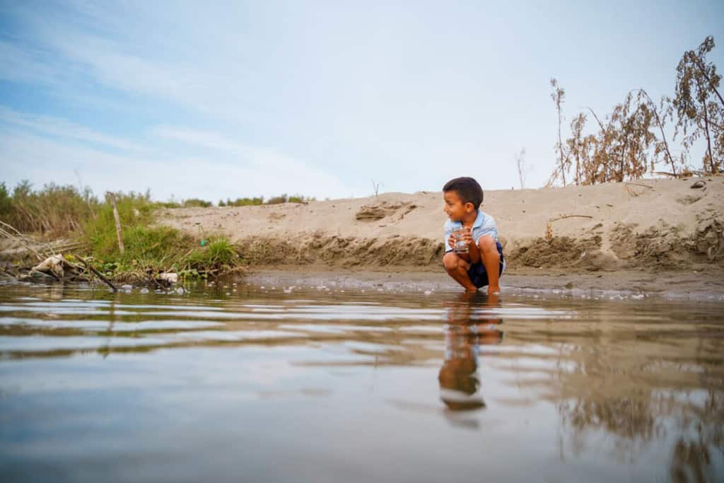 Un enfant est agenouillé au bord d'une rivière qui coule dans la communauté de Tamarindo.