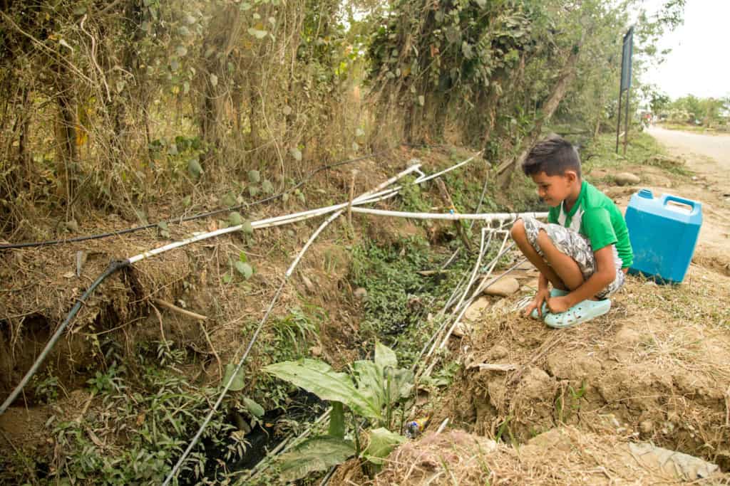 Garçon assis à côté de l'un des tuyaux de raccordement que les gens de sa communauté utilisent pour distribuer l'eau.