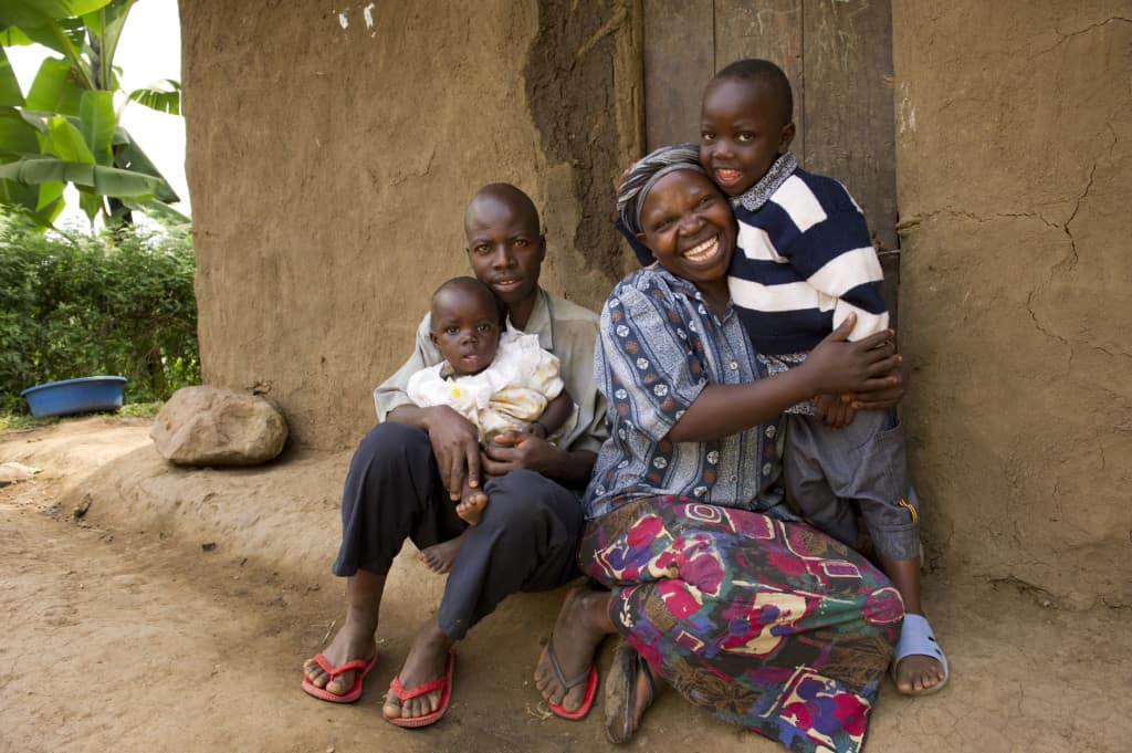 Hadija et son mari sont assis avec leur jeune fils et leur fille devant leur maison de terre en Ouganda