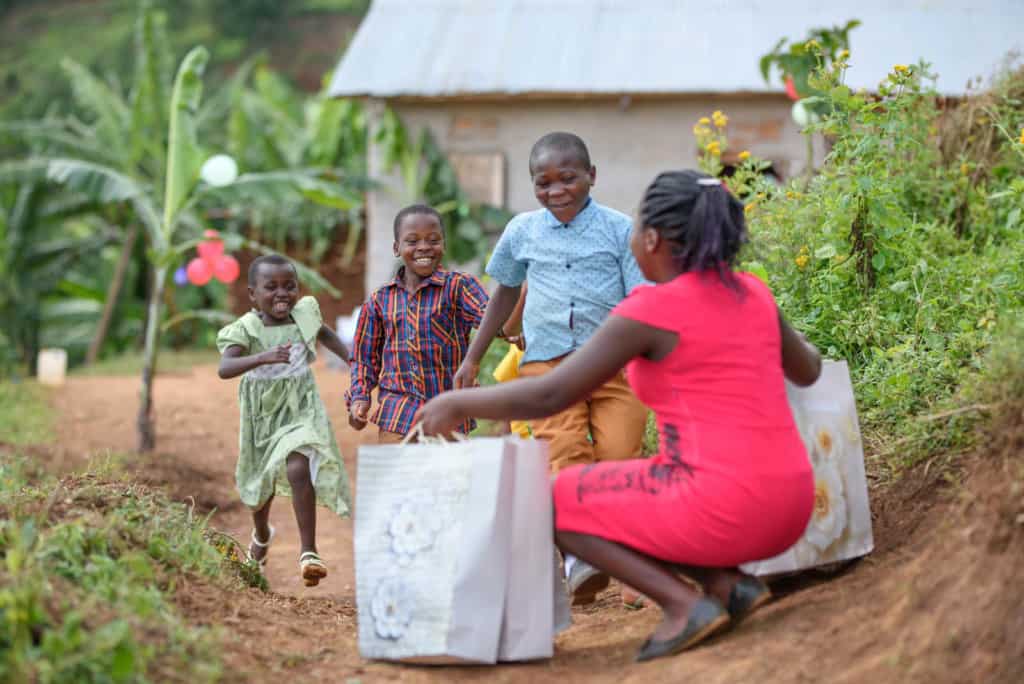 Livraison de cadeaux en Ouganda Martha porte une robe rouge et s'agenouille avec des sacs remplis de cadeaux de Noël pour les enfants. Un grand groupe d'enfants court vers elle.