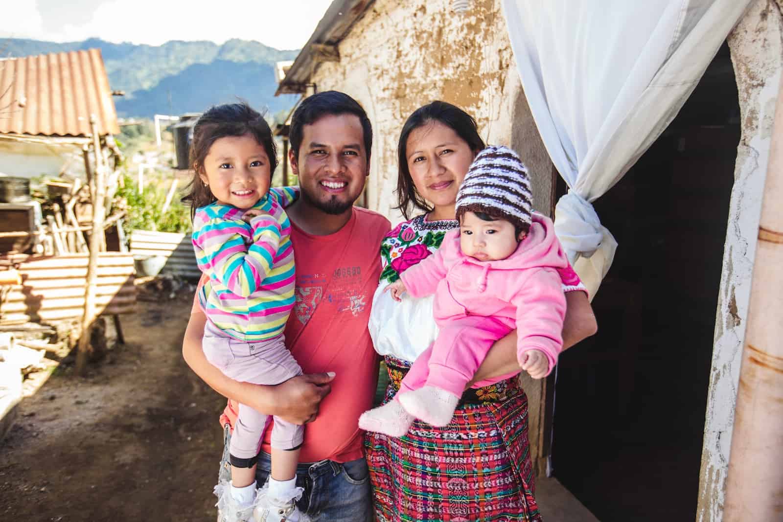 Une famille de quatre personnes devant une maison en brique au Guatemala.