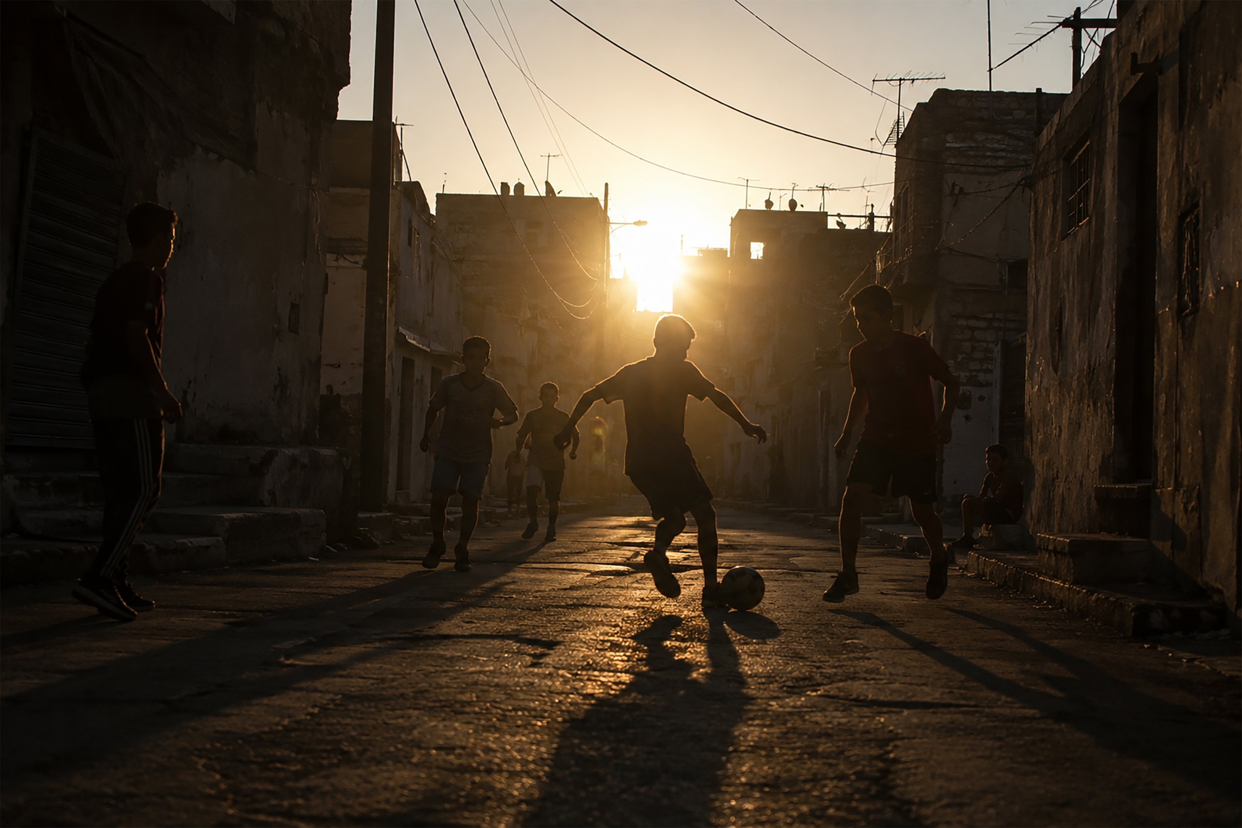 Silhouette d'un enfant jouant au football au coucher du soleil dans une rue. Des joueurs de football de la Coupe du monde qui ont grandi dans la pauvreté