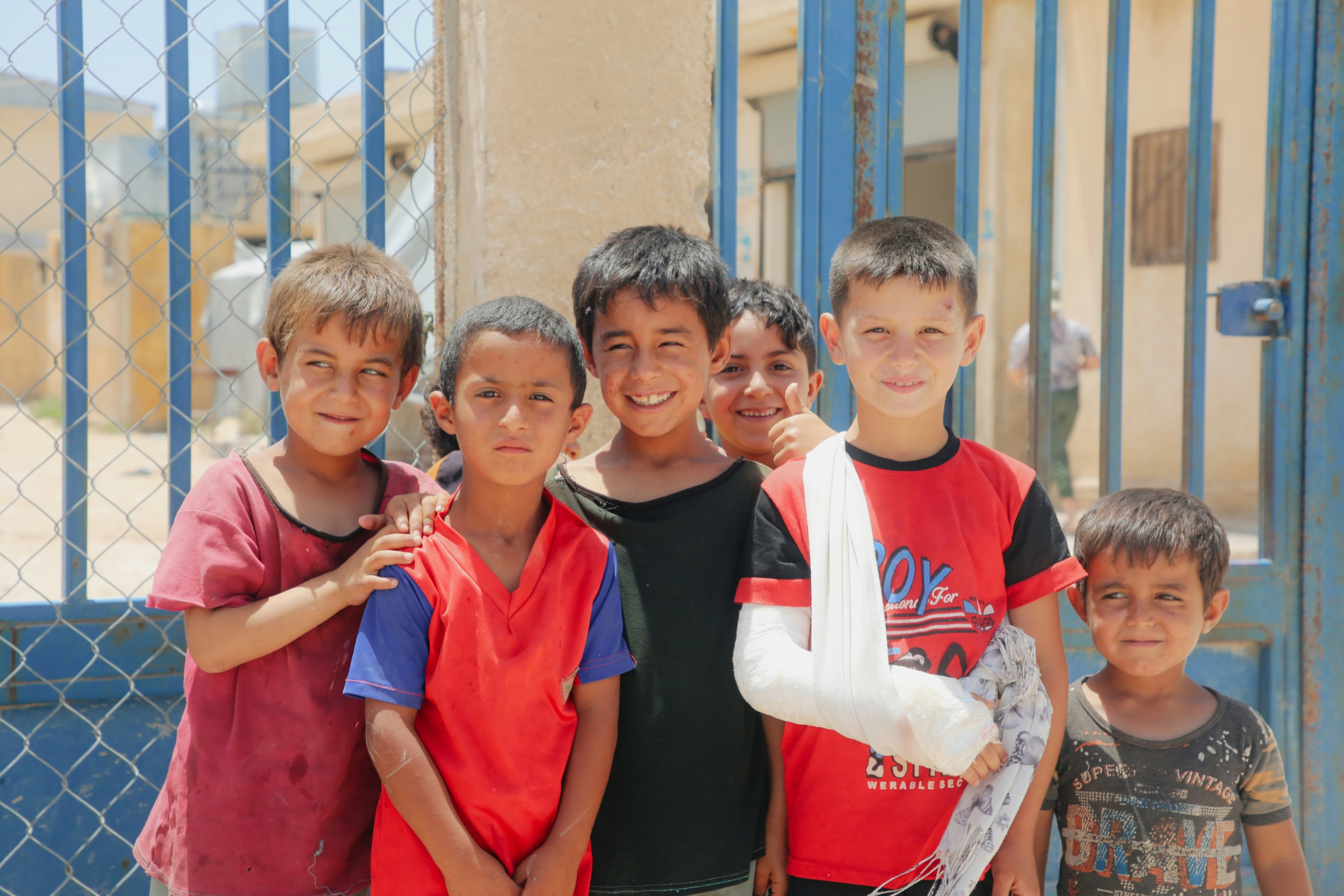 Un groupe de jeunes garçons debout ensemble, souriant à l’extérieur. Aide humanitaire du CCG