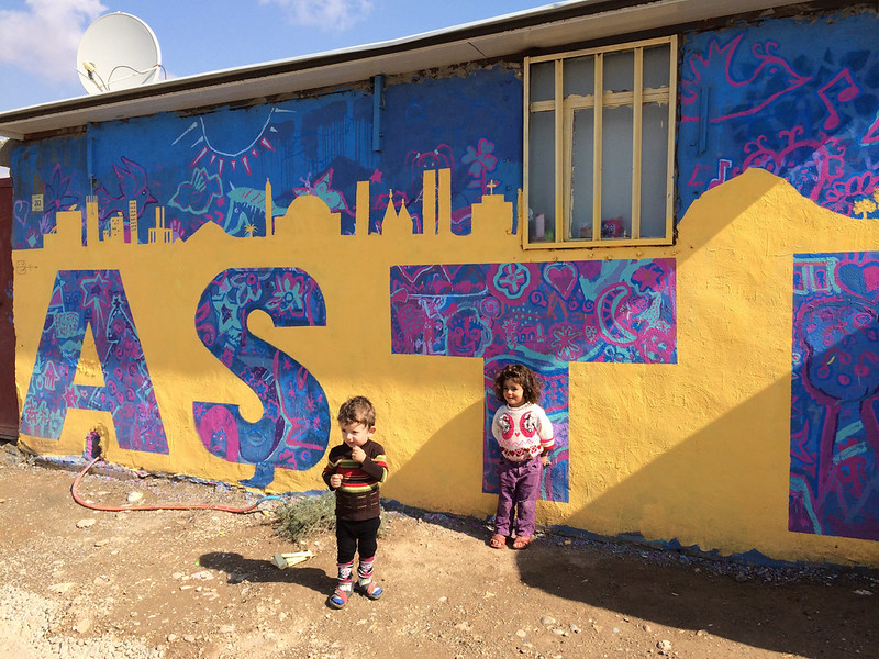 Groupe de personnes regardant une fresque murale vibrante ; partie des initiatives artistiques des réfugiés.